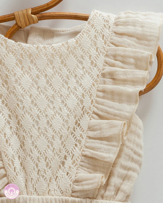 Close-up of beige cotton muslin romper with intricate lace panel and soft ruffle detail
