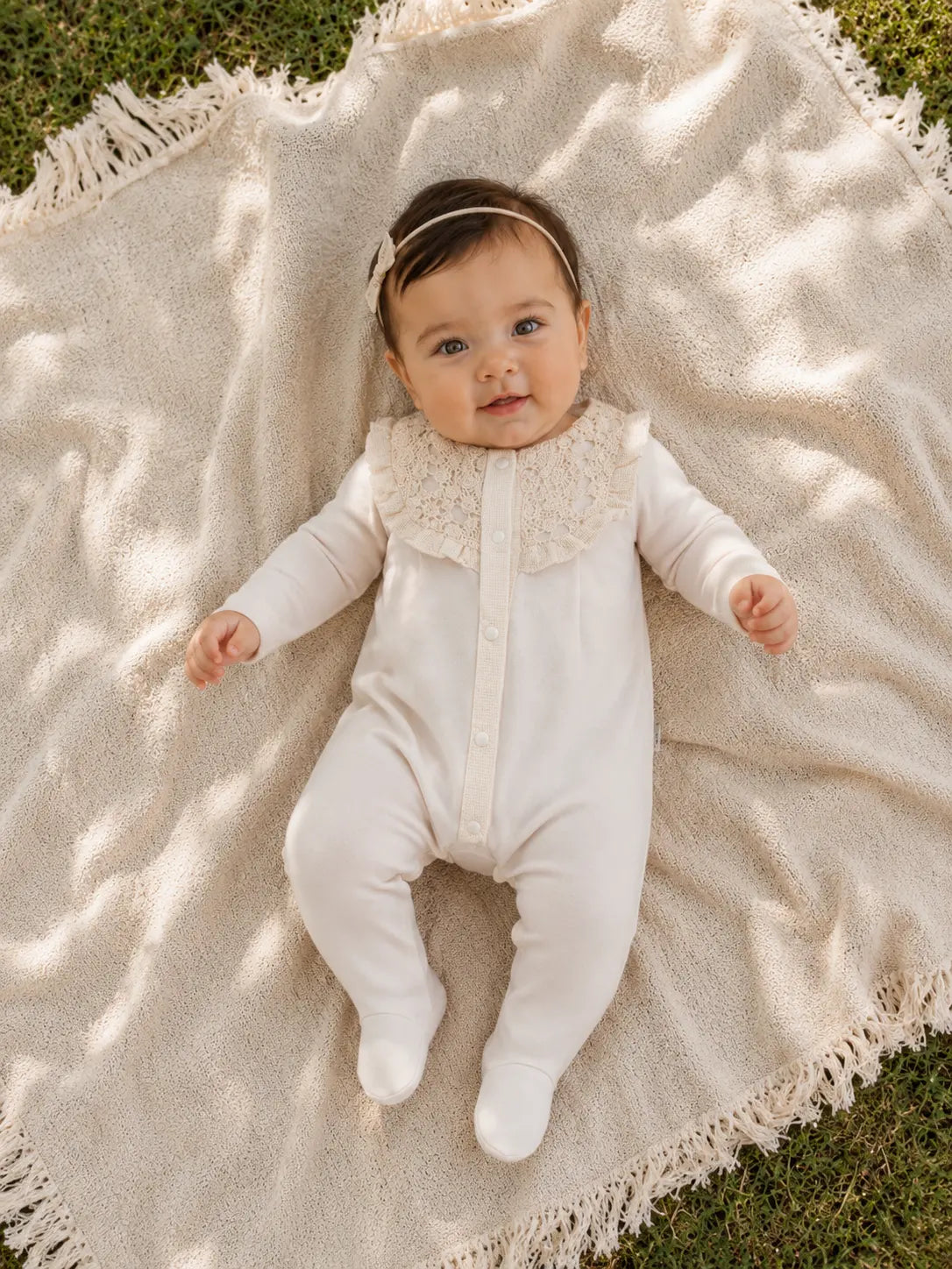 Newborn baby in elegant cotton romper with lace collar lying on blanket